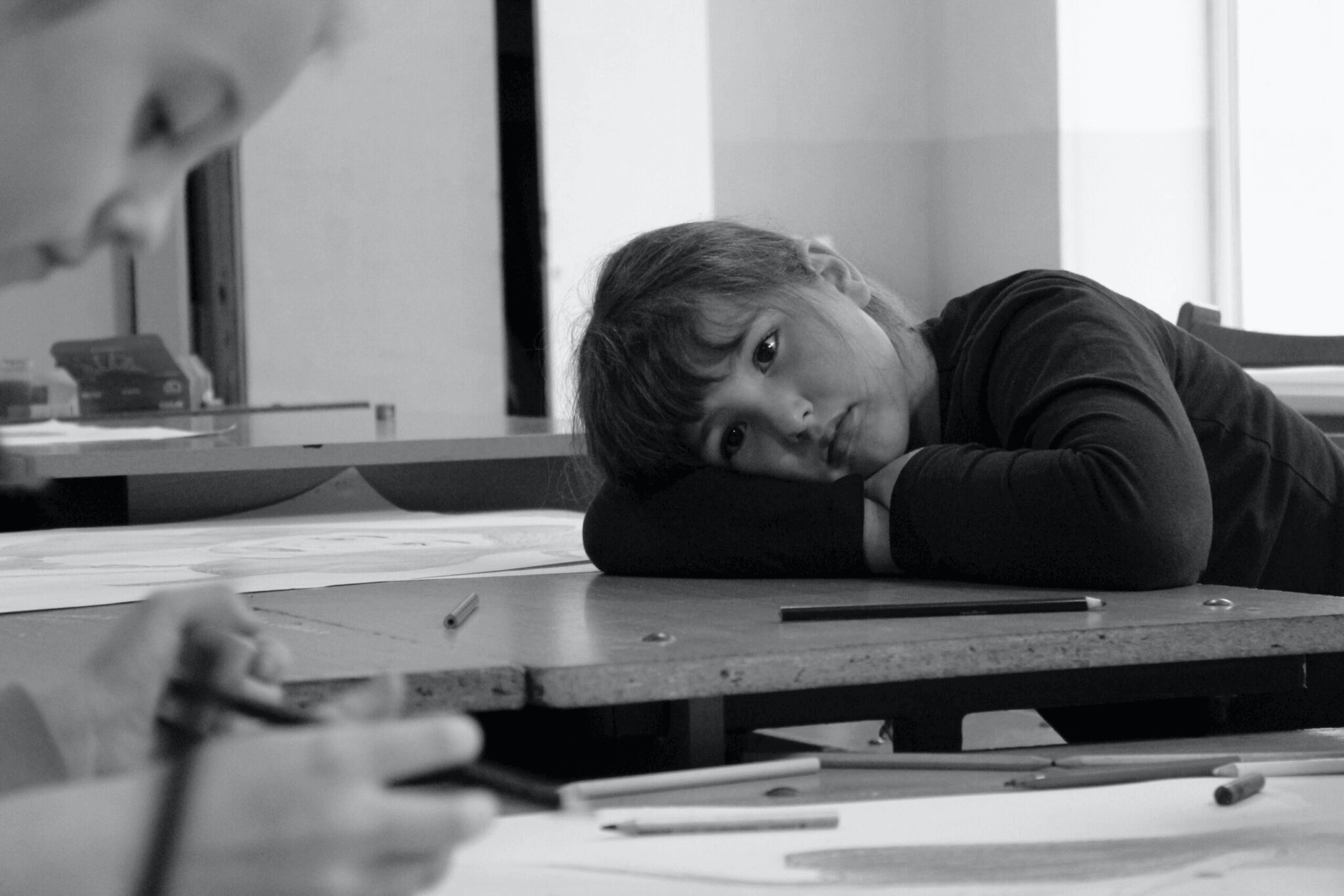 Black and white photo of a tired child resting on a school desk